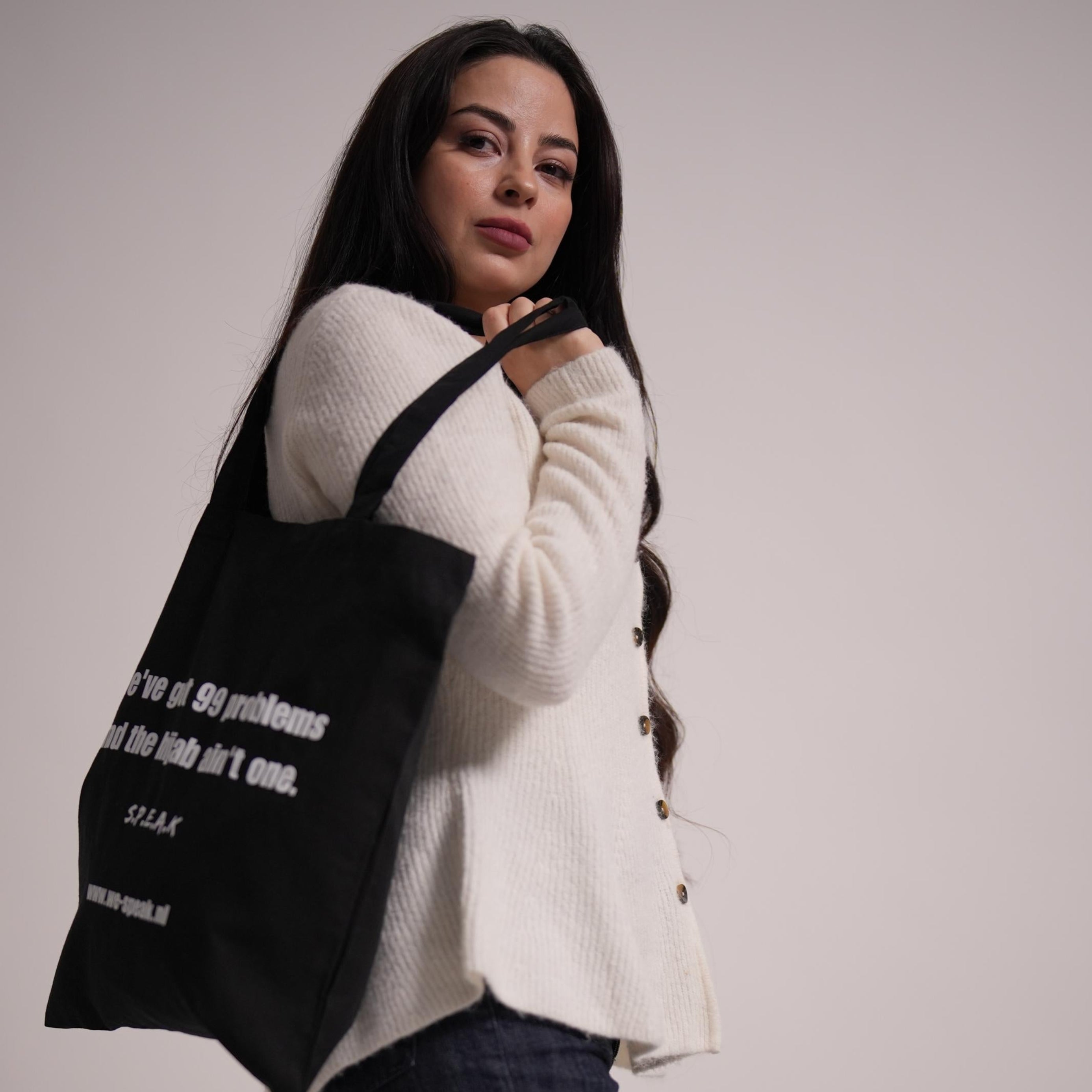Woman holding a black tote bag with text against a plain background